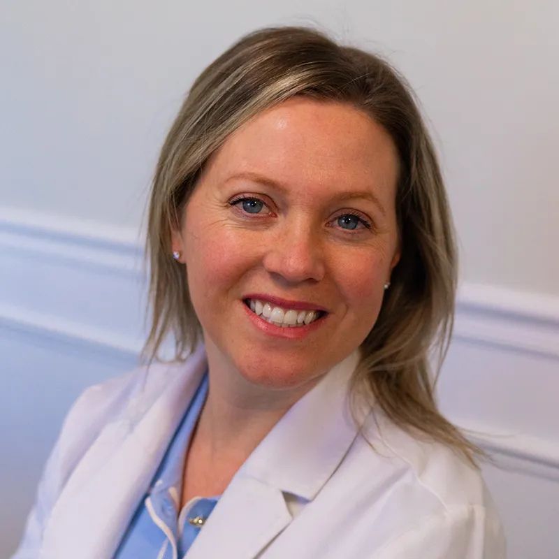 Dr. Rebecca Grome, audiologist, smiling in a white coat over a light blue shirt